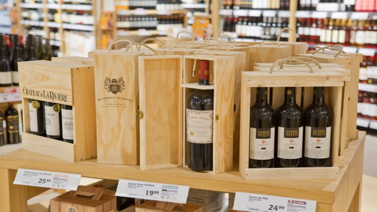 Mehrere Holzkisten mit Weinflaschen der Marken Château de La Rivière, Doppio Passo und Saveur du Midi auf einem Holztisch.