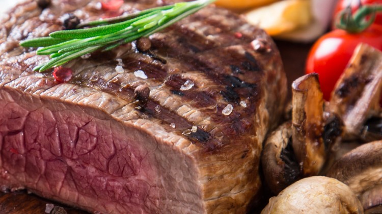 Ein aufgeschnittenes, medium gebratenes Steak mit Rosmarin, Pilzen, Kirschtomaten und Dipschalen im Hintergrund.