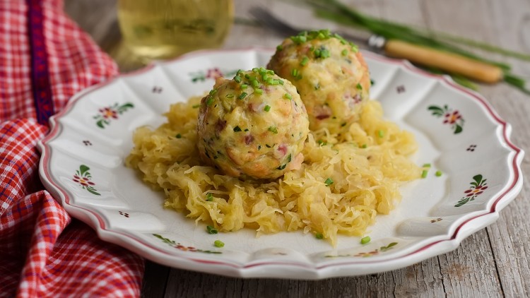 Zwei runde Knödel mit Schnittlauch auf Sauerkraut serviert, angerichtet auf einem Teller mit floralem Muster.