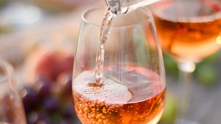 Ein Glas wird mit roséfarbenem Schaumwein gefüllt, im Hintergrund liegen Trauben und ein weiteres gefülltes Glas.