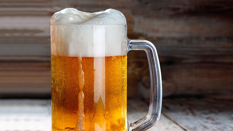 Ein Glas Bier mit goldener Flüssigkeit und weißem Schaum steht vor einem Hintergrund aus Holz.
