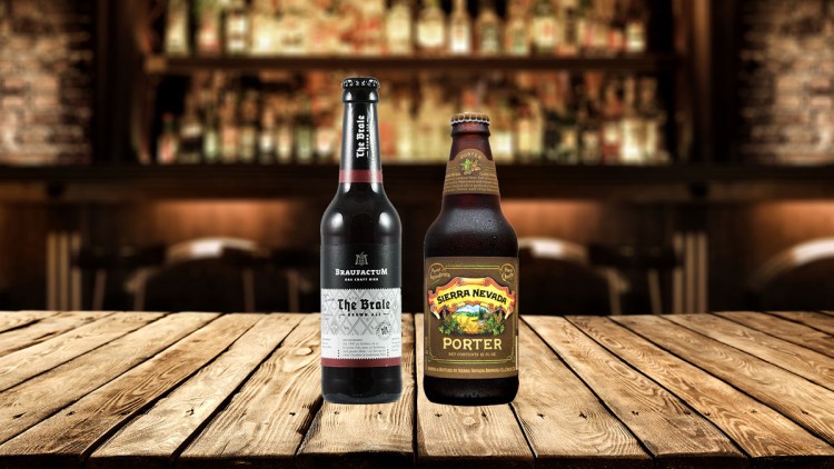 Zwei Bierflaschen, links Braufactum The Brale, rechts Sierra Nevada Porter, stehen auf einem Holztisch vor unscharfer Bar.