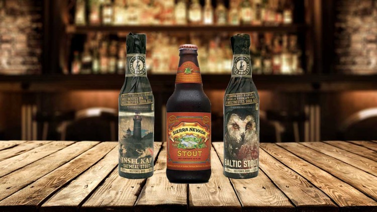 Drei Bierflaschen mit stilvollen Etiketten stehen auf einem Holztisch vor einer verschwommenen Bar als Hintergrund.