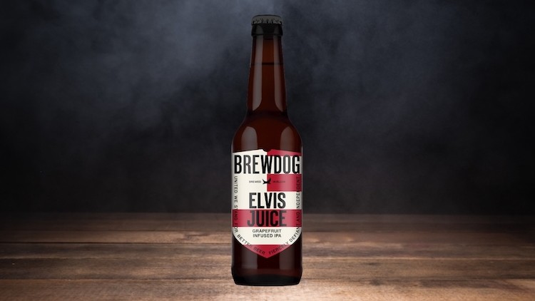 Braune Glasflasche mit rotem und weißem Etikett der Marke Brewdog, darauf der Schriftzug Elvis Juice, auf Holztisch vor dunklem Hintergrund.