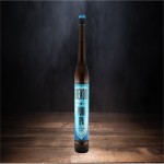 Braune Glasflasche mit langem Hals, blauem Verschluss und einem blauen Etikett auf einem dunklen Holztisch.