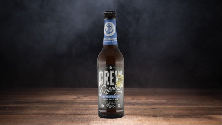 Braune Bierflasche mit blauem Etikett und der Aufschrift „CREW Republic Drunken Sailor India Pale Ale“, auf Holzuntergrund.