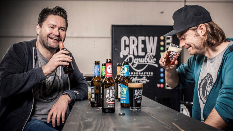 Zwei Personen sitzen an einem Holztisch mit Crew Republic Flaschen und Gläsern, im Hintergrund ein Crew Republic Schriftzug.