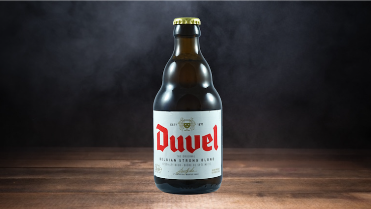Braune Glasflasche mit gelbem Kronkorken und weißem Etikett, darauf roter Schriftzug „Duvel“ und weitere Produktangaben.