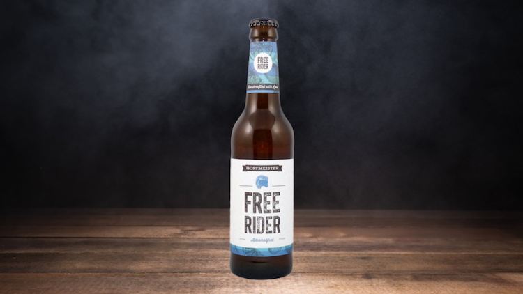 Braune Bierflasche mit der weißen Aufschrift „Hopfmeister Free Rider“ vor dunklem, leicht nebligem Hintergrund.