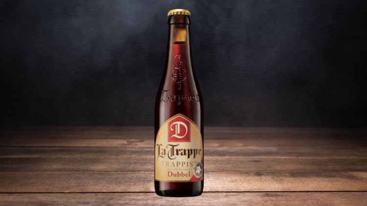 Braune Bierflasche „La Trappe Trappist Dubbel“ mit Etikett auf Holzuntergrund vor dunklem Hintergrund.