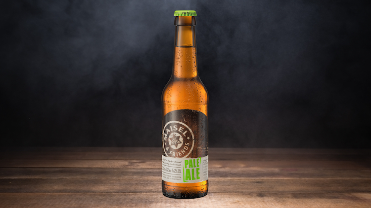 Eine braune Glasflasche mit grünem Kronkorken, dem Etikett „Maisel & Friends Pale Ale“ steht auf einem Holztisch vor dunklem Hintergrund.