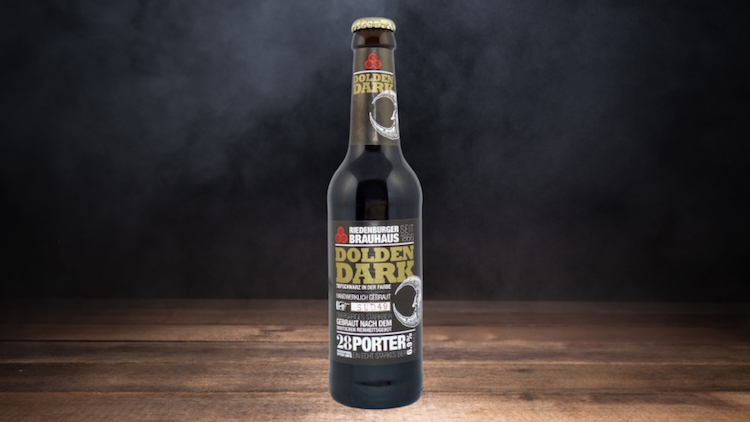 Braune Glasflasche mit goldenem Etikett und der Aufschrift „Golden Dark 23 Porter“ auf dunklem Holztisch vor schwarzem Hintergrund.