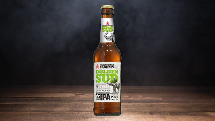 Braune Bierflasche mit der Aufschrift „Riedenburger Brauhaus Dolden Sud IPA“ steht auf Holzuntergrund vor dunklem Hintergrund.