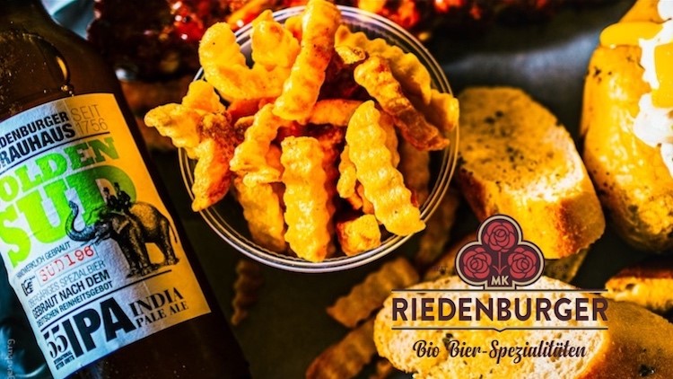 Wellenschneiden-Pommes in einer Schüssel, Riedenburger Bierflasche, belegte Brote und Logo „Riedenburger Bio Bier-Spezialitäten“.