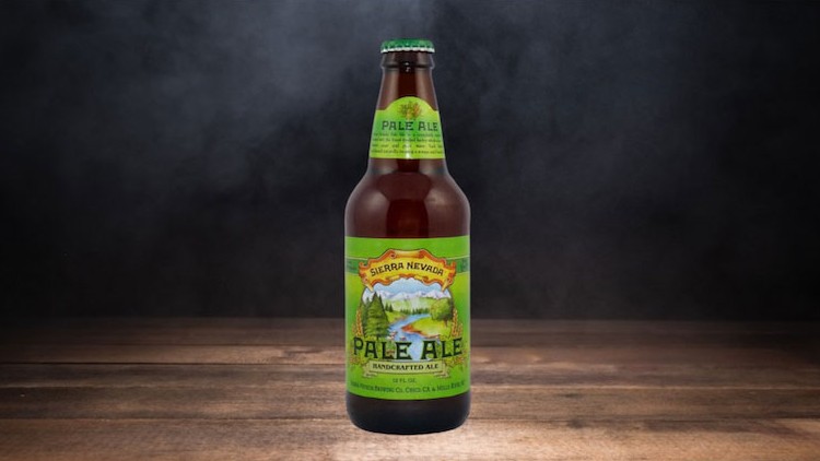 Braune Glasflasche mit grün-gelbem Etikett und der Aufschrift „Sierra Nevada Pale Ale“ auf Holzuntergrund, dunkler Hintergrund.
