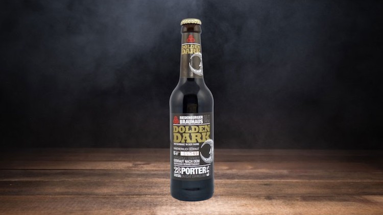 Schwarze Bierflasche mit der Aufschrift „Berliner Brauhaus Golden Dark 23 Porter“ steht auf einem Holztisch vor dunklem Hintergrund.
