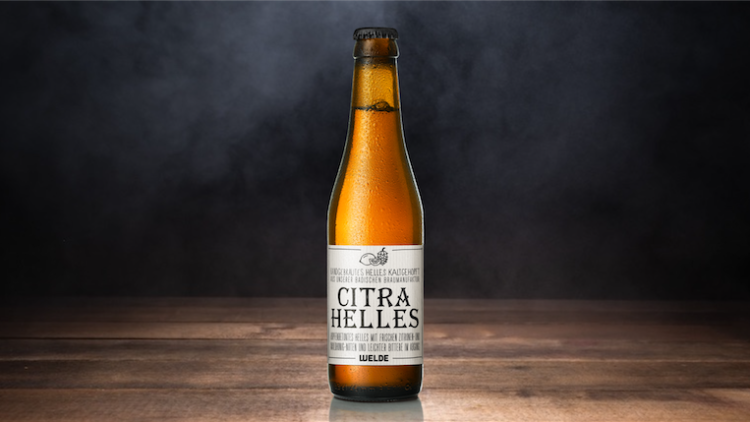 Eine braune Glasflasche mit der Aufschrift „Citra Helles“ steht auf einer Holzoberfläche vor einem dunklen Hintergrund.