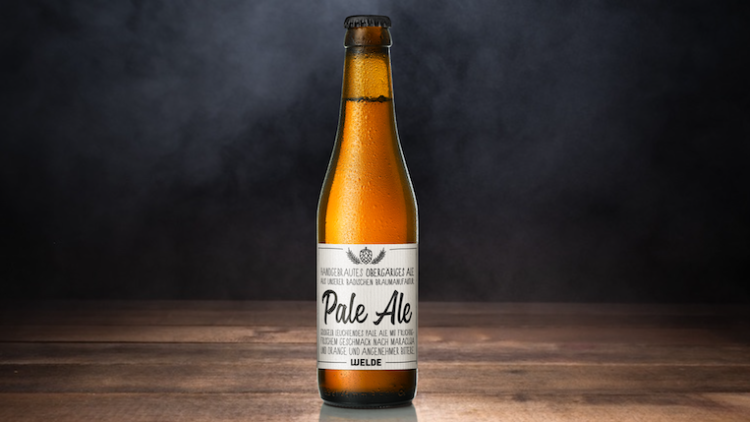 Braune Bierflasche mit der Aufschrift „Pale Ale“ steht auf einem Holzuntergrund vor dunklem, rauchigem Hintergrund.
