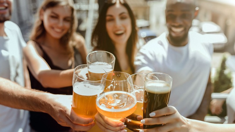 Mehrere Hände stoßen mit Gläsern gefüllt mit verschiedenen Getränken wie Bier und Schaumwein im Freien an.