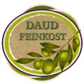 Grünes Logo mit Schriftzug „DAUD FEINKOST“, darunter grüne Oliven mit Blättern auf beigem Hintergrund und grün-lila Umrandung.