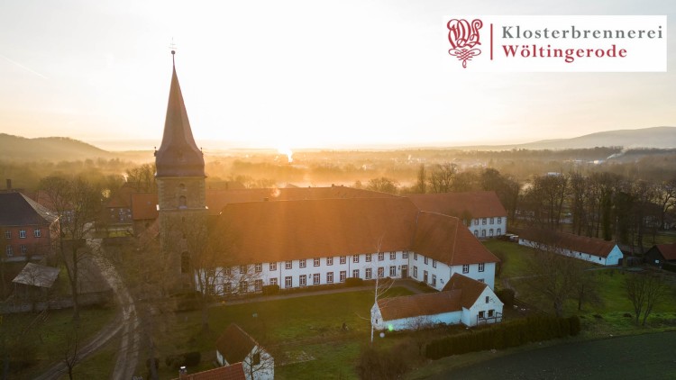 Luftaufnahme eines Klosters mit Kirche und roten Dächern bei Sonnenaufgang, Text: Klosterbrennerei Wöltingerode oben rechts.