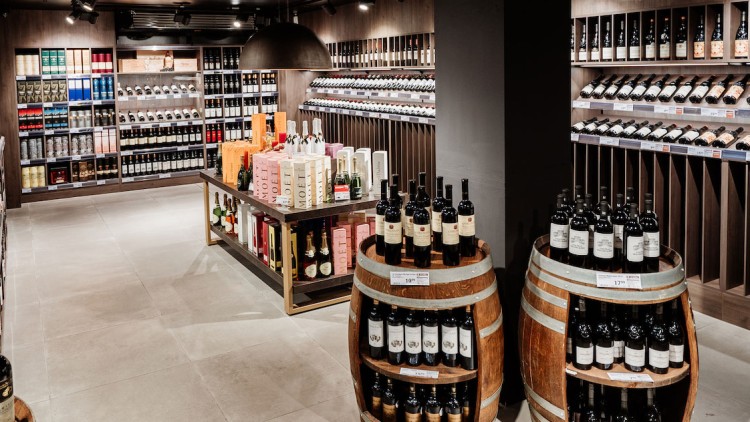 Ein gemütlicher Weinladen mit Regalen voller Weinflaschen, Holzböden, zwei Fässern und Geschenkpacks in der Mitte.