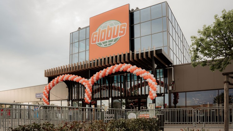Der Eingang eines GLOBUS Marktes mit Ballonbögen in Orange und Weiß, Glasfassade und einem Schild für FFP2-Maskenpflicht.