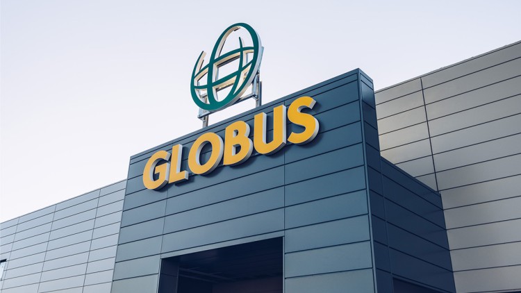 Blaues Gebäude mit gelbem GLOBUS-Schriftzug und grünem Logo auf dem Dach vor hellem Himmel.