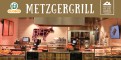 GLOBUS Metzgergrill mit beleuchtetem roten Kuh-Symbol, Theken mit Fleischwaren und Schriftzug „Von Hand mit Herz GLOBUS Metzgergrill“.