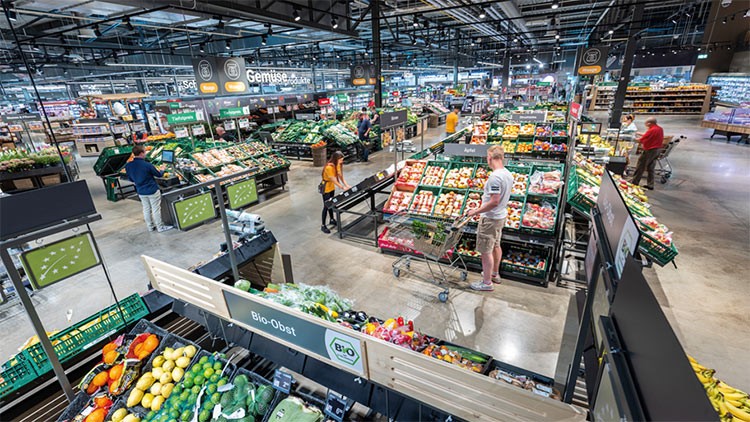 Menschen kaufen in einem GLOBUS-Markt Gemüse und Obst ein, mit Schildern wie „Gemüse“ und „Bio-Obst“ an den Regalen.