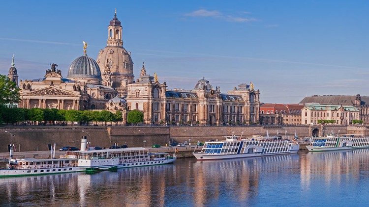 Panorama der historischen Altstadt von Dresden mit Elbe, Anlegestelle für Schiffe, Frauenkirche und weiteren Gebäuden bei klarem Himmel.