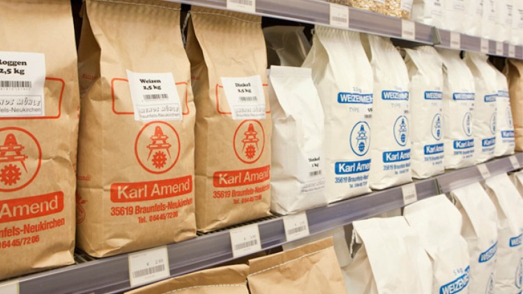 Papiertüten mit Mehl der Marke Karl Amend in Braun und Weiß stehen in Regalen, teils mit rotem oder blauem Logo bedruckt.