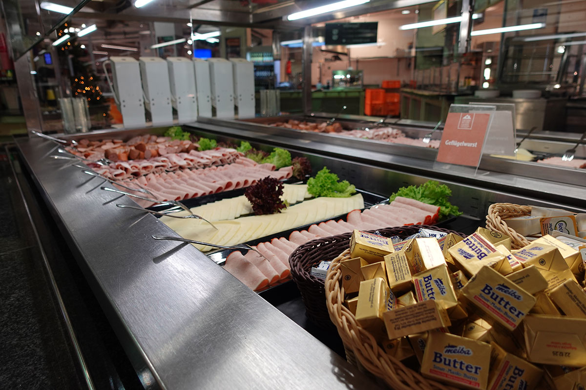 Eine Theke mit Geflügelwurst, Käse, Salat, einem Schild mit der Aufschrift „Geflügelwurst“ und Körben mit Butterstücken.