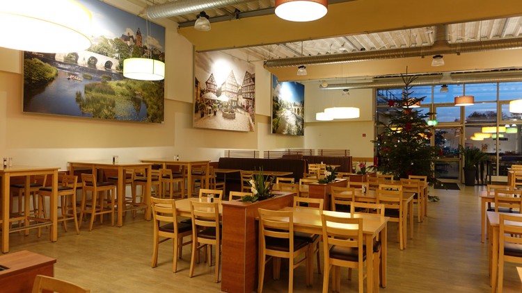 Ein heller Essbereich mit Holzmöbeln, Wandbildern und Weihnachtsbaum, beleuchtet von modernen Lampen und großen Fenstern.