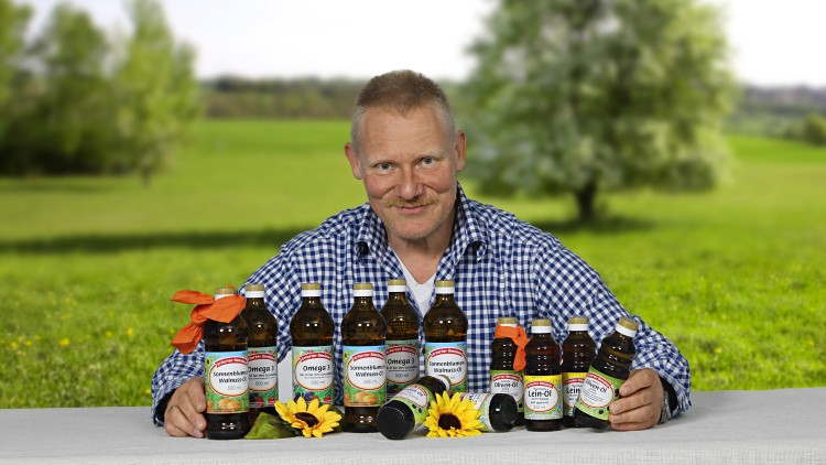 Mehrere braune Ölflaschen verschiedener Sorten stehen auf einem Tisch mit weißem Tuch, dekoriert mit Sonnenblumen.