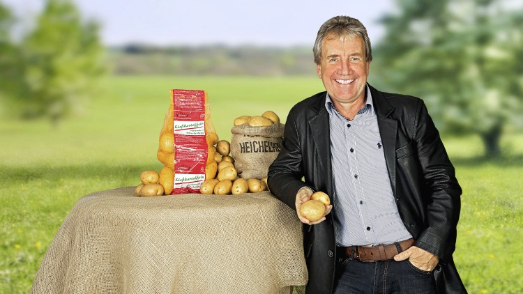 Ein Tisch mit Kartoffeln, einem Sack mit der Aufschrift „HEICHELSHOF“ und einer roten Verpackung mit der Aufschrift „Kleinkartoffeln“.