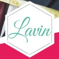 Weiße Fläche mit grünem Schriftzug Lavin in geschwungener Schrift, im Hintergrund Maßband und Stoff in Blau und Pink.