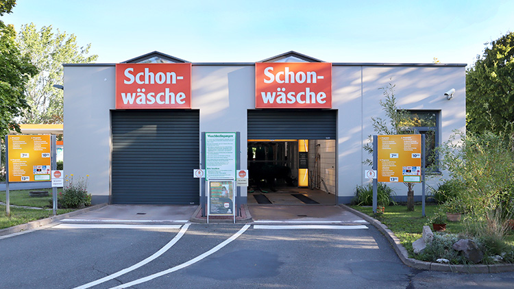 Waschhalle mit zwei Eingängen, darüber orange Schilder mit weißem Text \