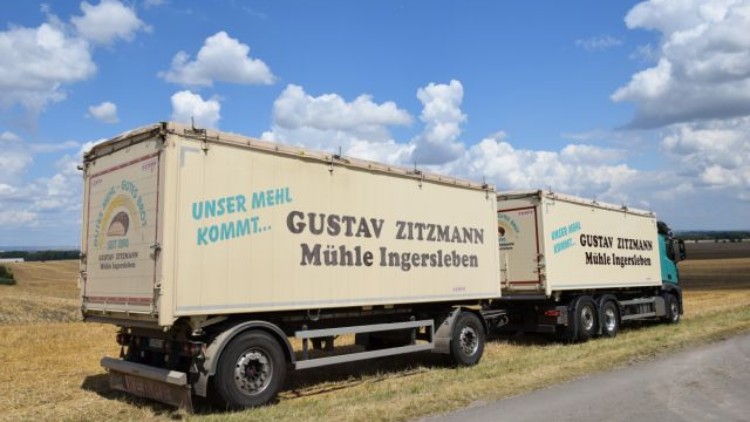 Ein Lkw mit der Aufschrift „Unser Mehl kommt… Gustav Zitzmann Mühle Ingersleben“ steht auf einem Feldweg vor Getreidefeldern.