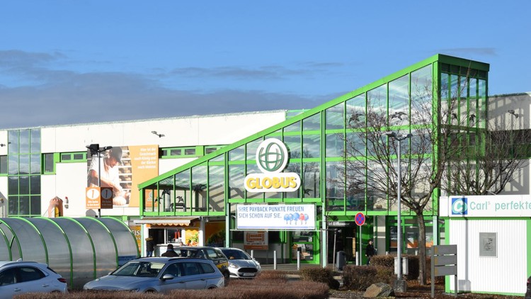 Eingangsbereich eines GLOBUS Marktes mit grünem Glasdach, Parkplatz, PAYBACK Hinweis und Werbebanner an der Fassade.