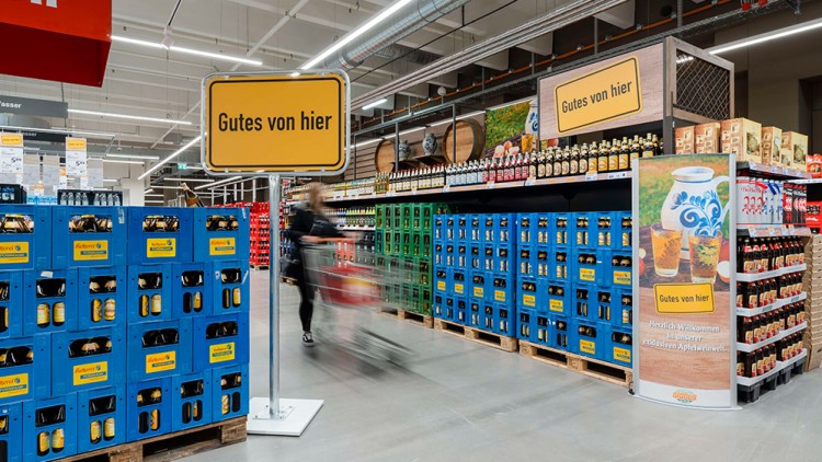 Regale mit blauen Getränkekisten, gelben Schildern „Gutes von hier“ und Werbesäule mit Apfelwein-Motiv im GLOBUS-Markt.