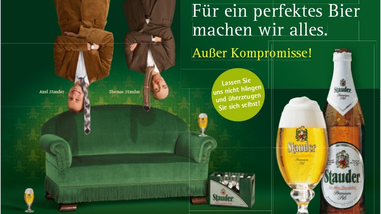Zwei Männer hängen kopfüber über einem grünen Sofa, daneben Bierflasche, Bierglas und Text: „Für ein perfektes Bier machen wir alles“.