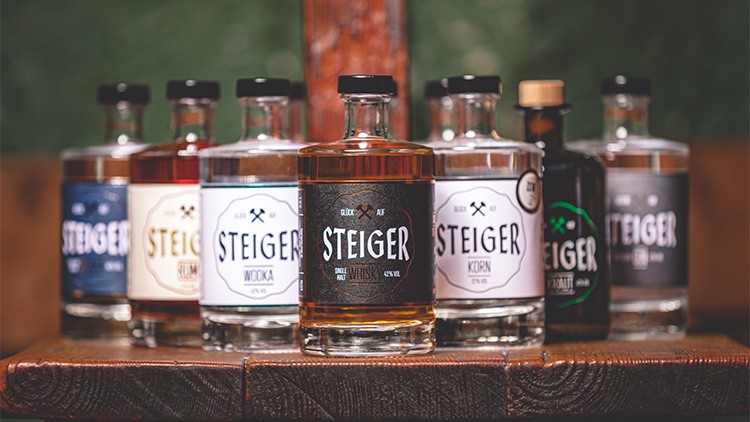 Verschiedene Steiger-Spirituosenflaschen, darunter Whisky, Wodka und Korn, stehen auf einem hölzernen Untergrund.