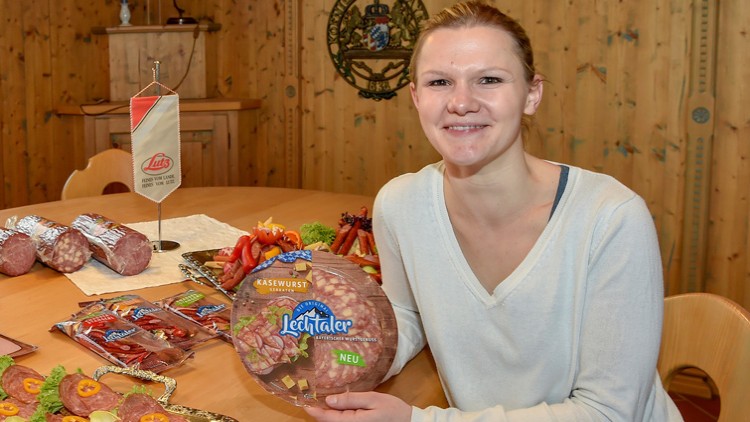Verschiedene Wurstwaren, darunter Lechtaler Käsewurst in einer Verpackung mit der Aufschrift „NEU“, auf einem Holztisch.