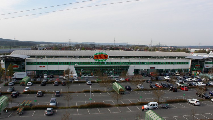 GLOBUS Markt mit großem Parkplatz, gläsernem Eingang, grün-weißem Gebäude und GLOBUS Logo auf der Fassade.
