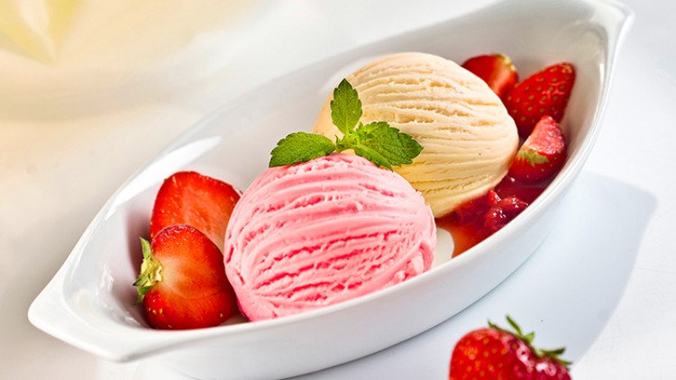 Zwei Kugeln Eiscreme in Rosa und Beige mit frischen Erdbeeren und Minzblatt auf weißem Teller angerichtet.