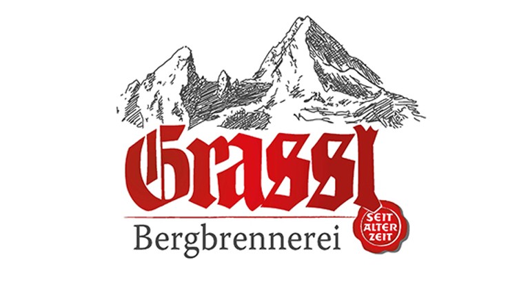 Logo mit den Worten „Grassl Bergbrennerei“ in Rot und Schwarz, gezeichnete Berge im Hintergrund, rechts ein rotes Siegel „Seit alter Zeit“.