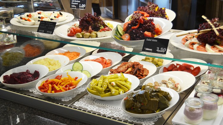 Frische Salatbar mit Schalen gefüllt mit Antipasti, eingelegtem Gemüse, Salaten, Wraps, Joghurt-Desserts und Preisschildern.