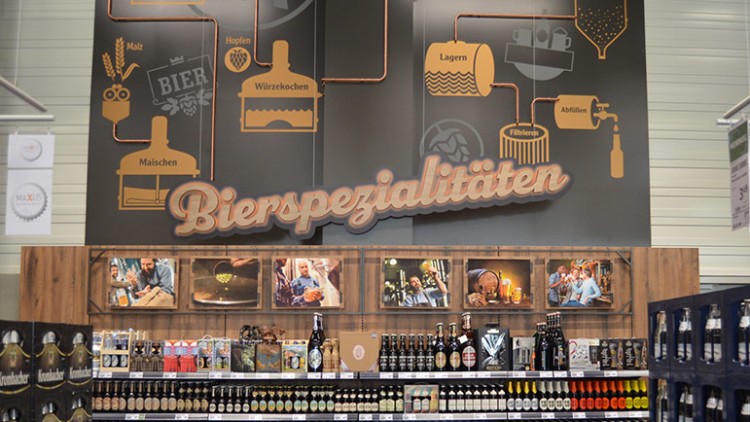 Regale mit verschiedenen Biersorten, darüber ein Schild mit der Aufschrift Bierspezialitäten und Illustrationen zur Bierherstellung.