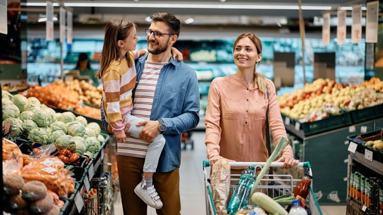 Eine Familie mit Einkaufswagen steht in der Obst- und Gemüseabteilung eines Supermarkts mit verschiedenen frischen Produkten.